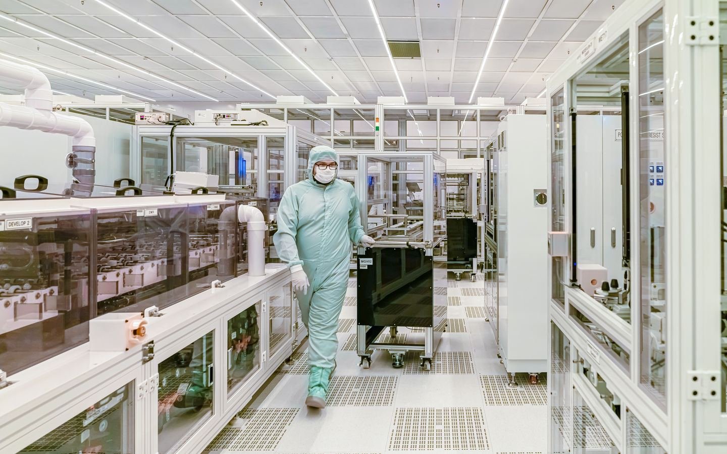 Technician in protective clothing working inside a clean laboratory environment.