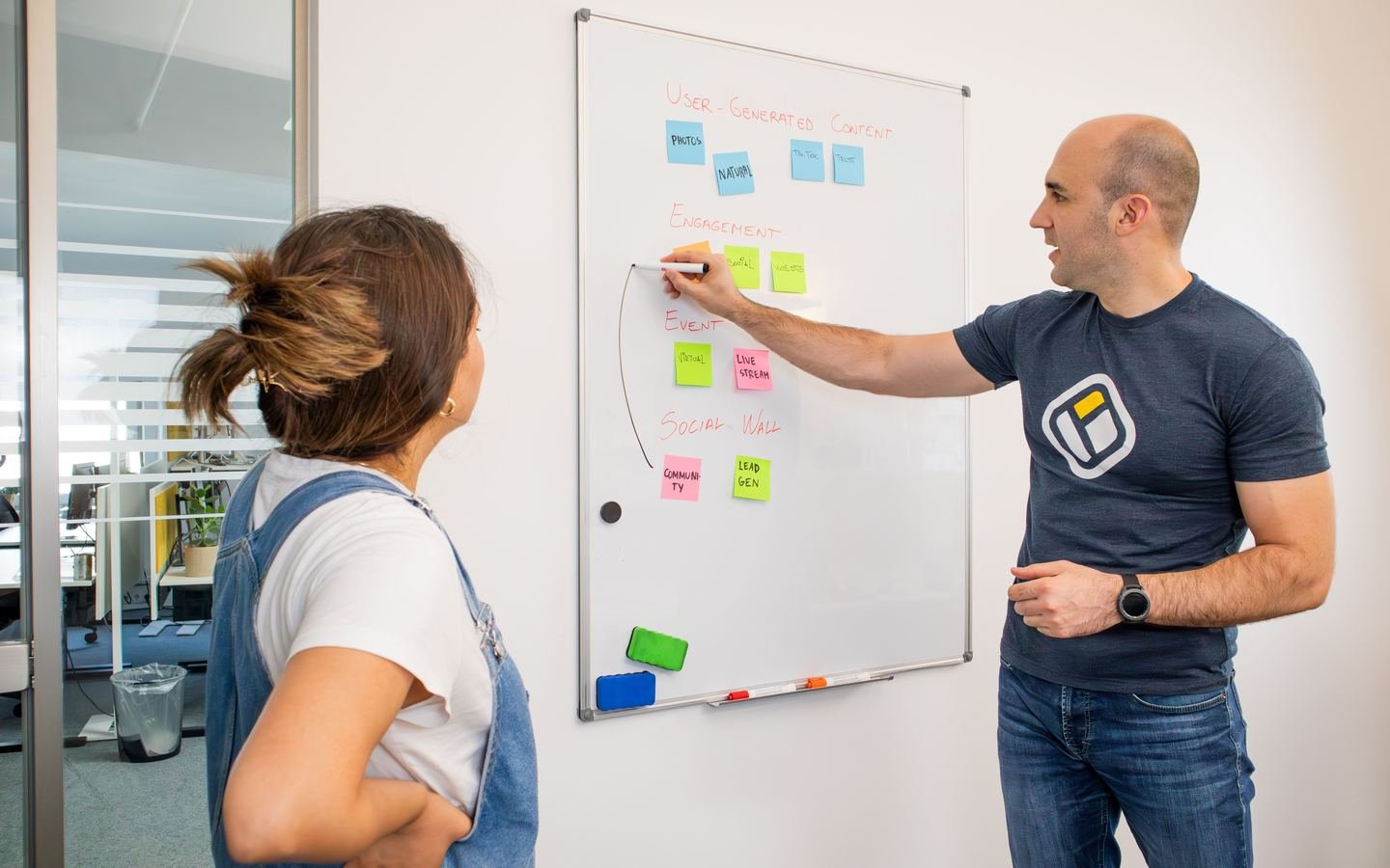 Two colleagues planning project work using notes on a whiteboard.