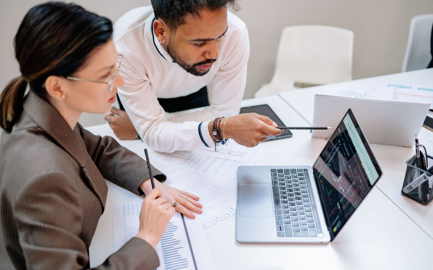 Two professionals reviewing business data and charts on a laptop.